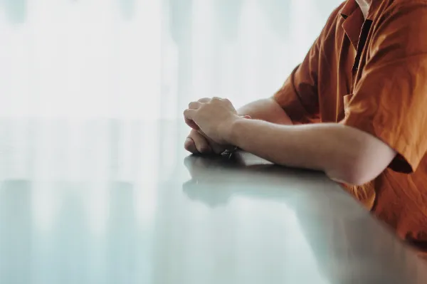 ALTはじまり:テーブルに腕を置いて座る葉栗さんの手元のアップ。オレンジ色のシャツを着用。 ALTおわり