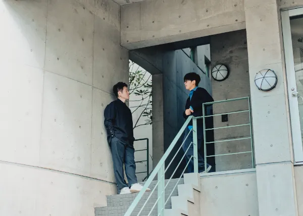  写真：建物の階段踊り場で向かい合い、立ち話をする井上さんと松野さん。