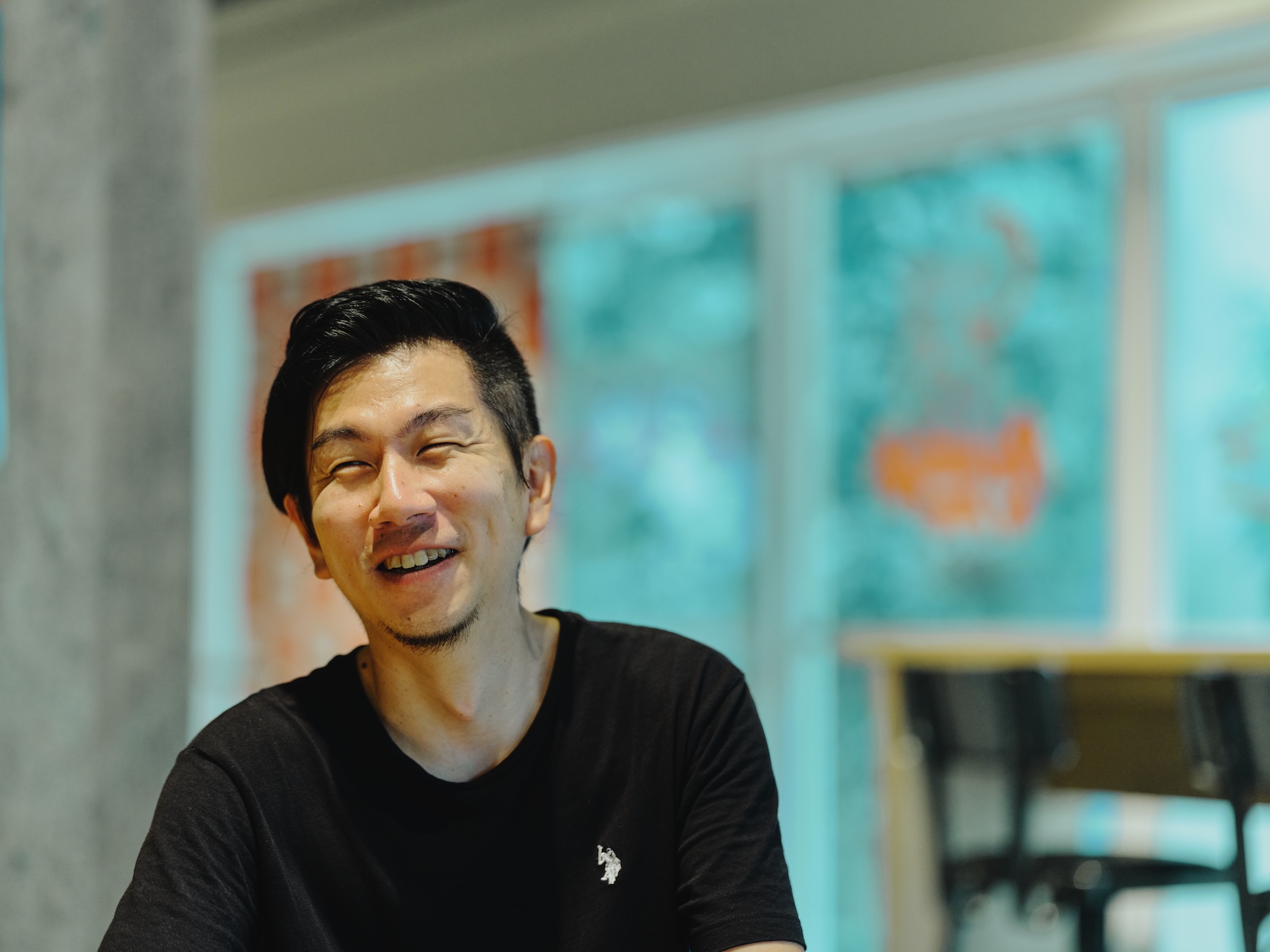 ALTはじまり:陽の光が当たる明るい場所で、目を細めて心から笑っている溝口さんのバストアップ写真です。ALTおわり