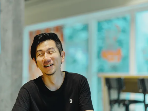 ALTはじまり:陽の光が当たる明るい場所で、目を細めて心から笑っている溝口さんのバストアップ写真です。ALTおわり