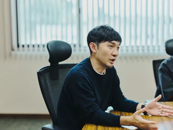 写真:藤原印刷の藤原隆充さんが発言している様子。黒いニットを着て、手を広げながら説明している。