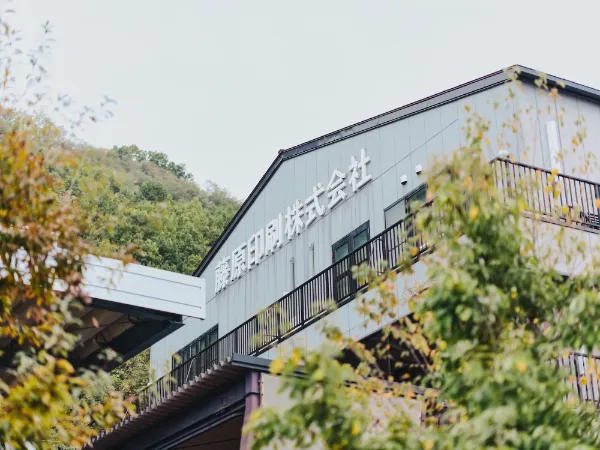 写真:長野県松本市にある藤原印刷株式会社の外観。社名看板が掲げられ、周囲には木々が広がっている。