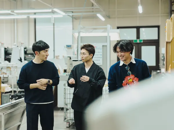 写真:工場内を歩きながら話す藤原隆充さんとnovactの尾木洸太さん、速水駿さん。印刷現場を見学しながら意見を交わしている。