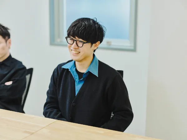  写真：笑顔を見せる松尾さん。会議中の和やかな一瞬を捉えたカット。