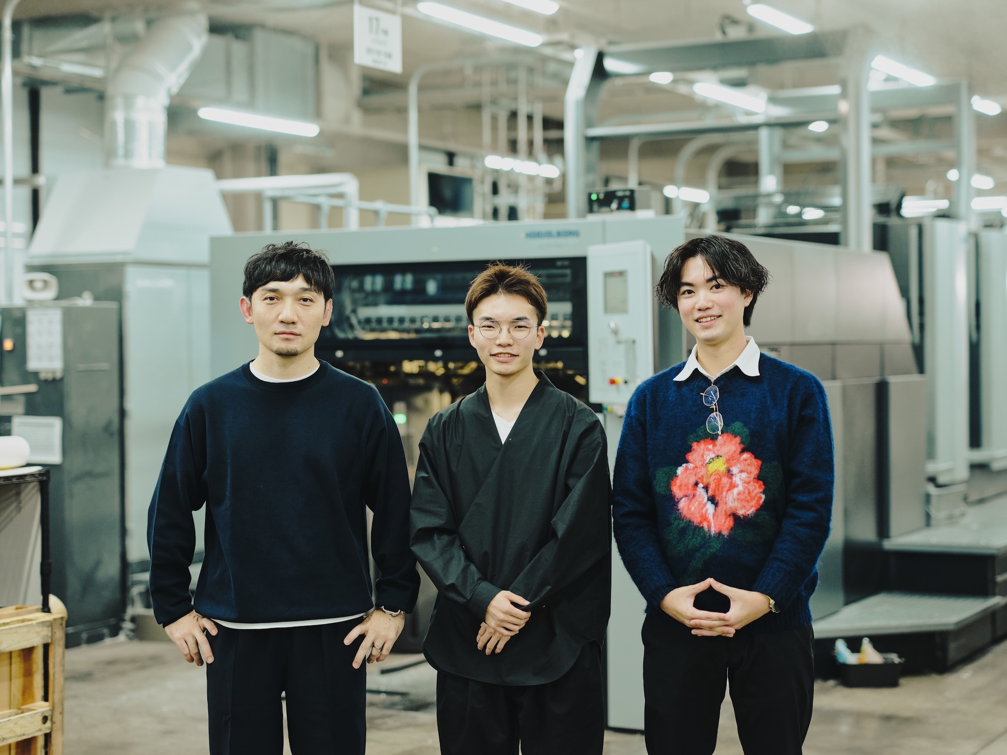 写真:工場の印刷機前で並ぶ藤原隆充さん、尾木洸太さん、速水駿さん。新サイト制作をともに進めた3名のおだやかな表情。