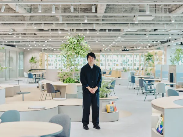  ALTはじまり：植栽が多く開放的な共創LOUNGEの中央に立つ兼原さんの全身像。ALTおわり