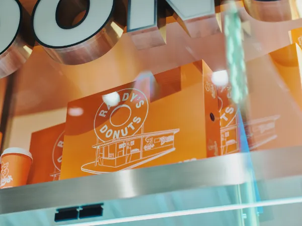 ALTはじまり:ガラスのショーケース越しに置かれた「RANDY'S DONUTS」のロゴが大きく描かれたオレンジ色の箱。ALTおわり