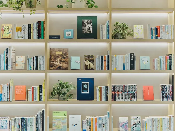 ALTはじまり:温かい光に照らされた、書籍と観葉植物が並ぶ共創LOUNGEの本棚。ALTおわり