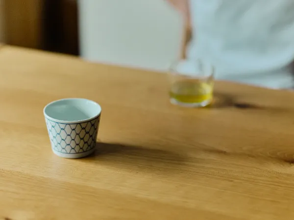 ALTはじまり: 木製のテーブルに置かれた蕎麦猪口とお茶の入ったグラス。ALTおわり