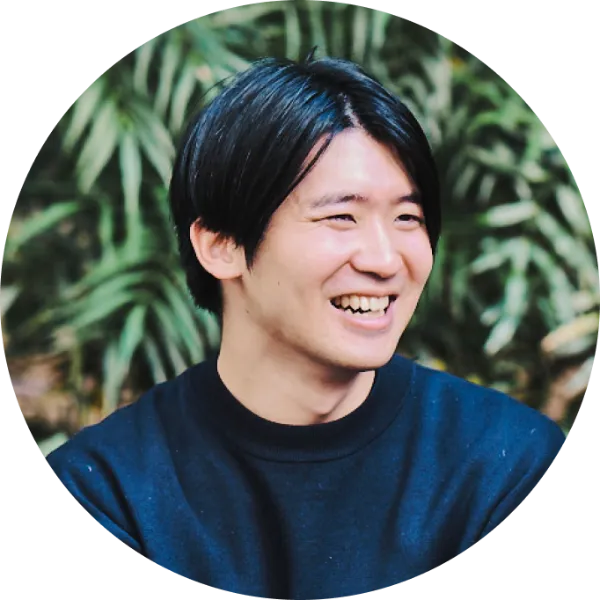 ALTはじまり:屋外で撮影した、少し横を向きながら笑っている高橋鴻介さんのプロフィール写真。黒いスウェットを着て、リラックスした雰囲気。背後には柔らかな緑が広がっている。ALTおわり