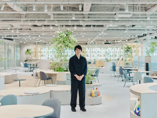 ALTはじまり:植栽が多く開放的な共創LOUNGEの中央に立つ兼原さんの全身像。ALTおわり