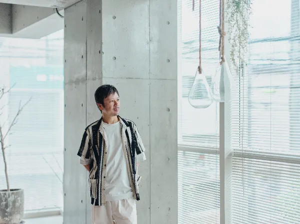 ALTはじまり: ベイジのオフィスで、コンクリートの柱と大きな窓を背景に立つベイジ代表の枌谷力さん。ALTおわり