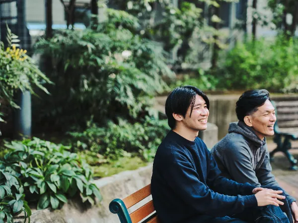 ALTはじまり:公園のベンチに並んで座り、笑顔で談笑している石井さんと高橋さん。落ち着いた緑の背景の中、和やかな雰囲気が伝わる。ALTおわり