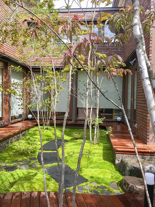 苔の築山、石畳、そして奥へと続くウッドパスが調和する中庭。異なる素材を組み合わせた奥行き感のある造園デザイン。