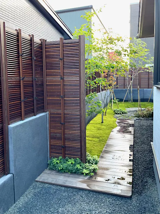 竹垣風のフェンスとコンクリート壁で囲まれたプライベートな庭。緩やかな曲線を描くウッドデッキの通路と美しい苔庭。