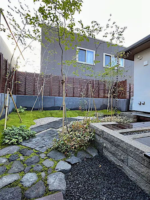 高低差を活かした石積みと植栽のレイアウト。黒い砂利と苔、落葉樹のコントラストが美しい庭園の全景。