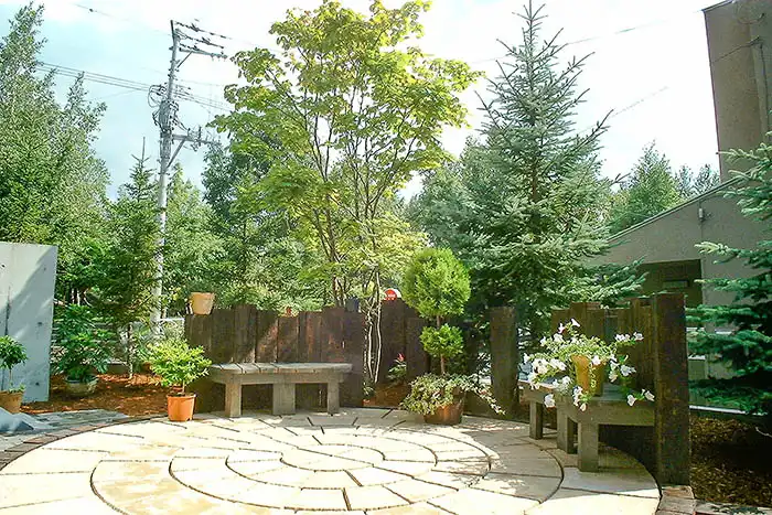 円形に敷き詰められた石畳のテラスと木製ベンチを組み合わせた庭の休憩スペース