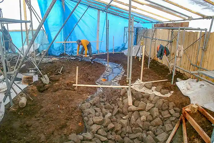 緩やかにカーブする水路の溝に沿って、黒い遮水シートが隙間なく丁寧に敷設されている様子。