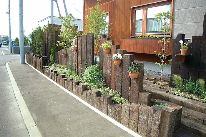 アンティークな枕木を高さ違いで並べたおしゃれな土留めとハンギングバスケットで飾られた花壇