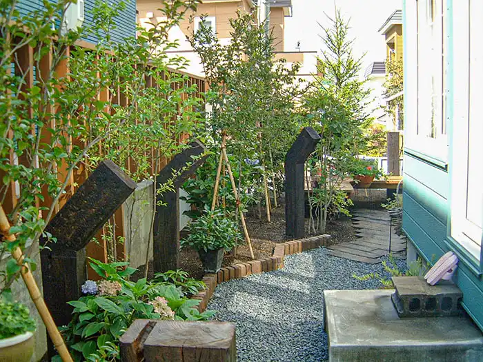 住宅の勝手口から続く砂利敷きの通路に枕木のオブジェと植栽を配置したナチュラルな外構デザイン