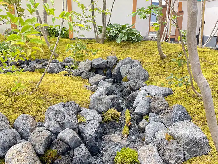 一面を覆う美しい苔の絨毯(じゅうたん)を切り裂くようにデザインされた、力強い石組みの流路。