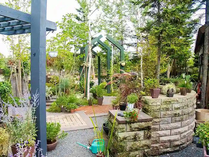 曲線を描く石積みの壁と、奥に見える独特な形の木製アーチ。青いじょうろが置かれた手入れの行き届いた売場。