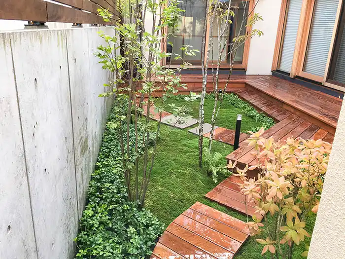 建物を取り囲むL字型の濡れ縁と、そこから続く曲線的なウッドパス。足元には豊かな苔と下草が広がる、潤いのある中庭。