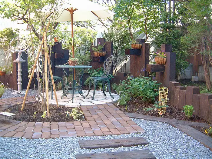 白いガーデンパラソルの下に置かれたテーブルセットと枕木の土留めで囲まれたテラス