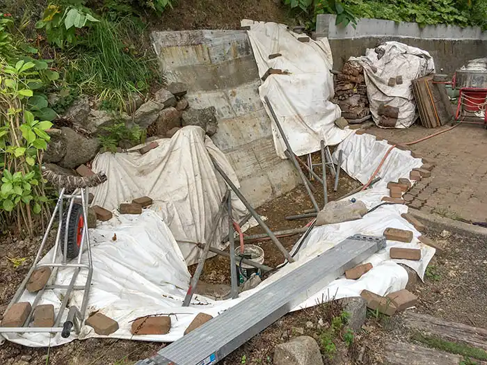 池の土台となる部分を掘削し、全体に白い防水シートを敷き詰め、石やレンガで固定している作業工程。