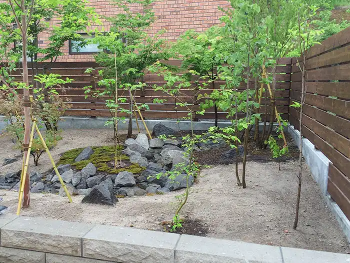 自然な高低差をつけた土壌に、景石と部分的な苔の張り込みが行われている庭づくりの様子。