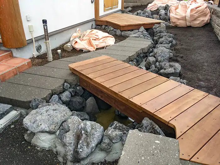 完成に近い木製デッキが水路（流れ）をまたぐように設置されている。デッキの下を水が通る構造になっており、周囲の石組みも整えられている。