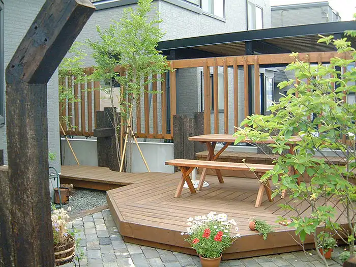 変形ウッドデッキに木製のベンチとテーブルを設置したプライベート感のあるアウトドアリビング