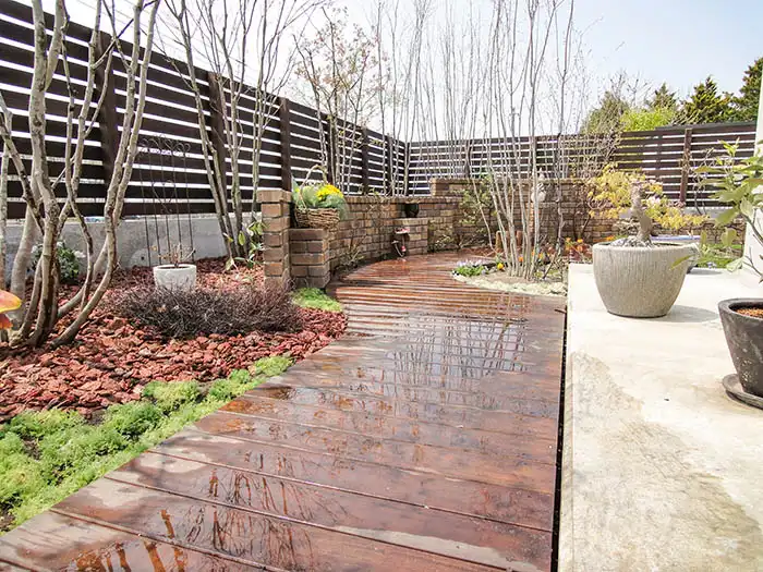 ウッドデッキの小道に沿って配置されたバークチップのマルチングとシックな横張りウッドフェンス