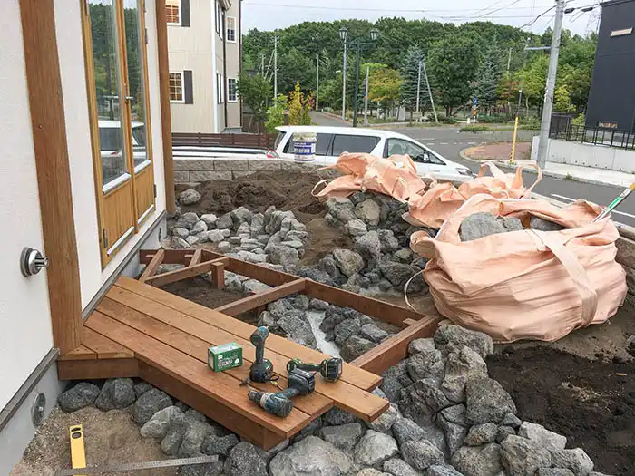 デッキの床板が一部張られ、インパクトドライバーなどの工具が置かれている。周囲ではさらに石が積み上げられ、庭の形が立体になってきている。