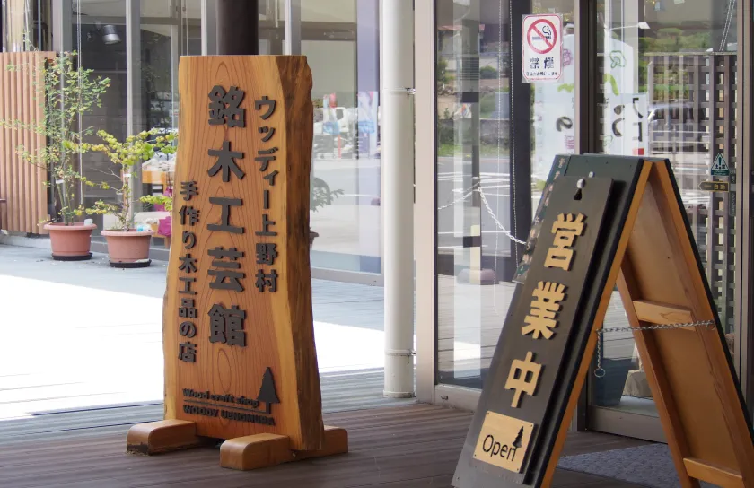 ウッディー上野村銘木工芸館と書かれた大きな木製看板があるエントランス