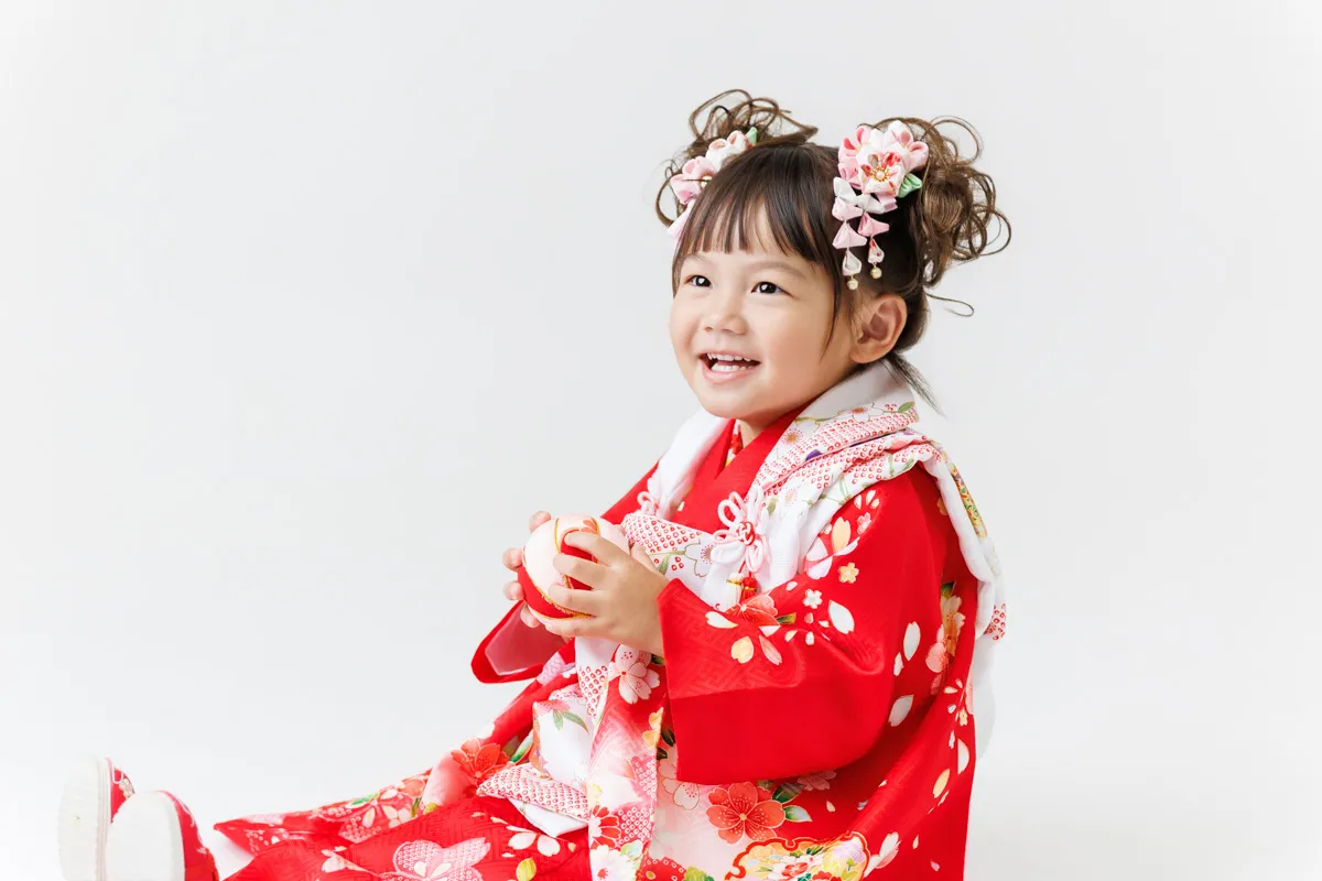 赤い被布姿で座って笑う3歳の女の子|能美市の七五三