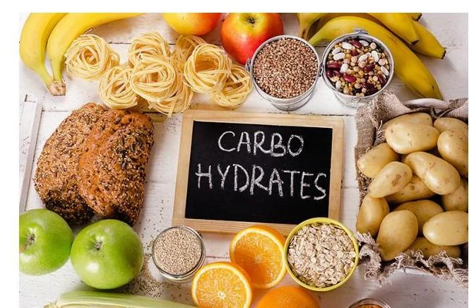 A collection of foods rich in carbohydrates, including bananas, pasta, bread, buckwheat, beans, potatoes, oranges, and oats.