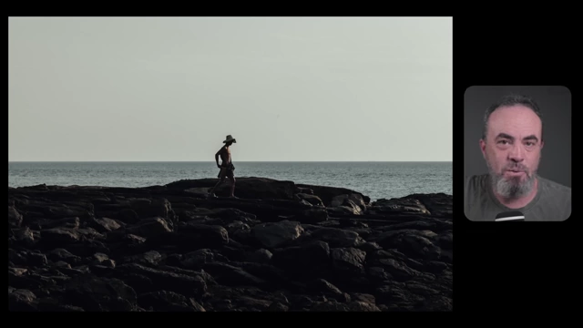 A man stands firmly on dark rocks by the sea under a light sky, illustrating a composition that feels natural and balanced.