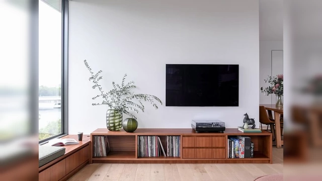 A modern living room with a TV mounted above a long, wooden console table that extends beyond the width of the screen, creating a balanced and visually grounded setup.