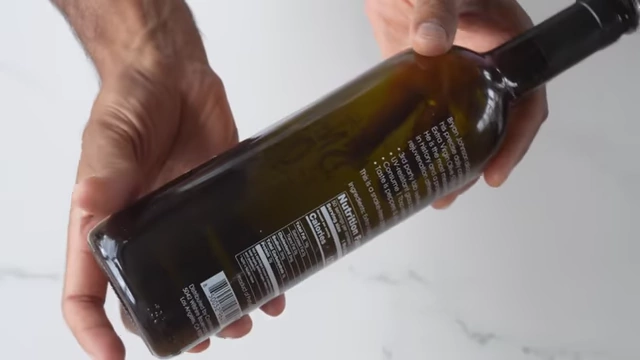 A dark glass olive oil bottle with nutrition information and ingredients on the label is shown.