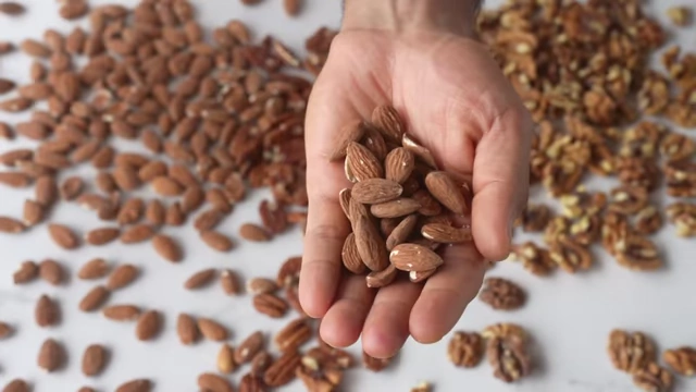 A hand holds a small bowl of mixed nuts, including almonds and walnuts.
