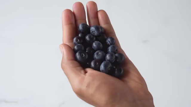 A hand holds a small pile of blueberries.