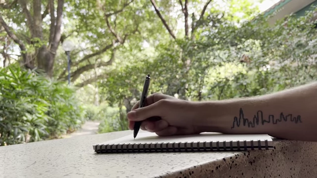A person's arm with a skyline tattoo, writing in a notebook