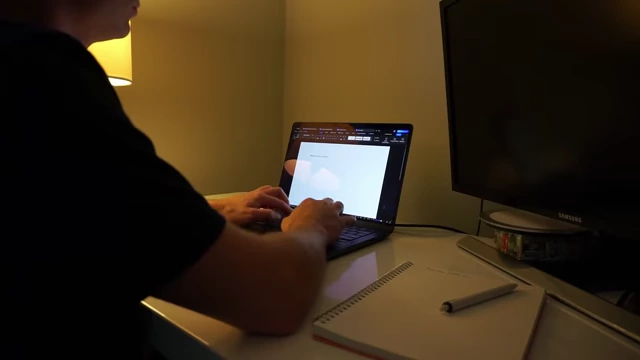 A person typing on a laptop in a dimly lit room