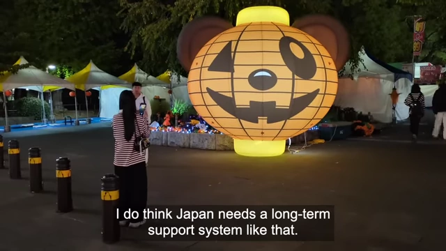 A person with a Halloween-themed lantern, with text reading "I do think Japan needs a long-term support system like that.", suggesting a need for more sustainable solutions.