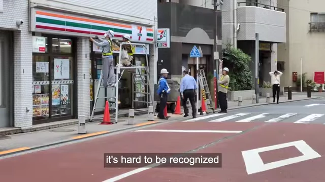 Workers outside a 7-Eleven with text "it's hard to be recognized as a person in Japan", emphasizing the societal pressure to work for validation.