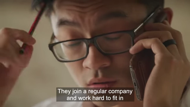 A man working hard at his desk with text overlay: "They join a regular company and work hard to fit in", highlighting the pressure to conform in the workplace.