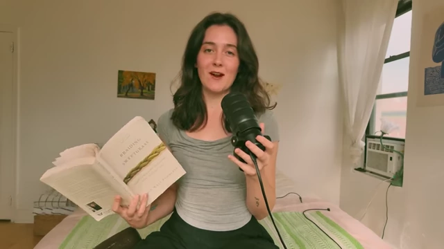 The speaker holds a copy of Robin Wall Kimmerer's 'Braiding Sweetgrass'.
