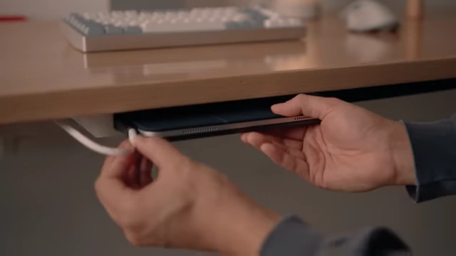 Hand inserting an iPad with a charging cable into an under-desk custom holder