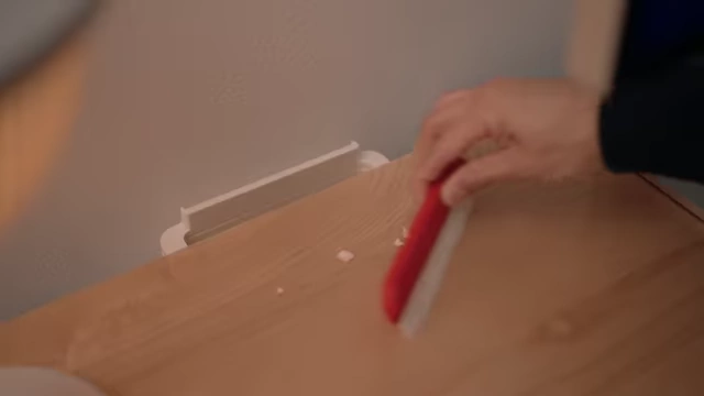 Hand using the red removable part of the trash bin system as a brush on the desk